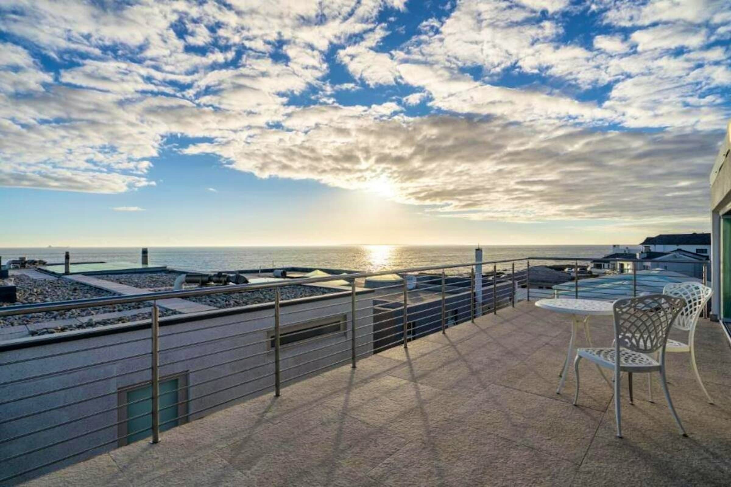 Ocean-facing terrace with outdoor chairs beneath a clouded sky
