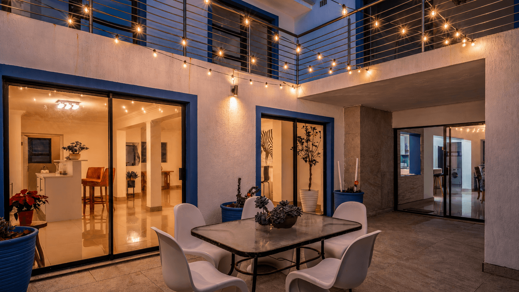 The Lighthouse courtyard at blue hour, framed in cobalt with warm festoon lights.